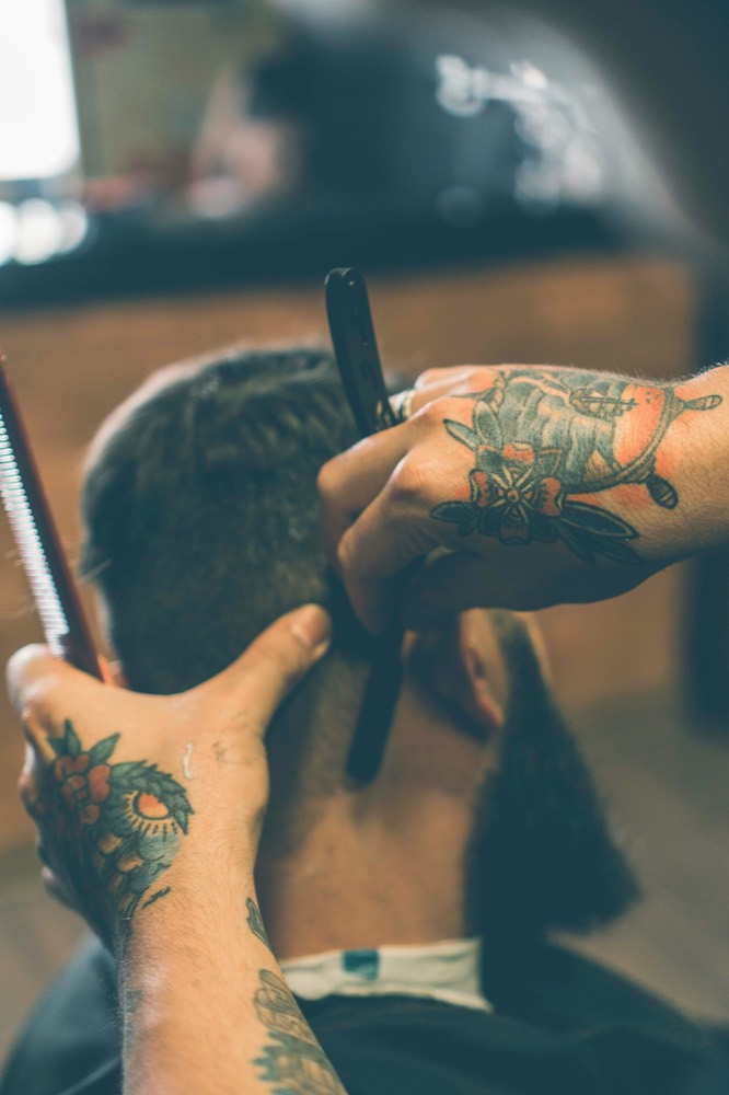 Tattooed barber lining up a hairline with a straight razor