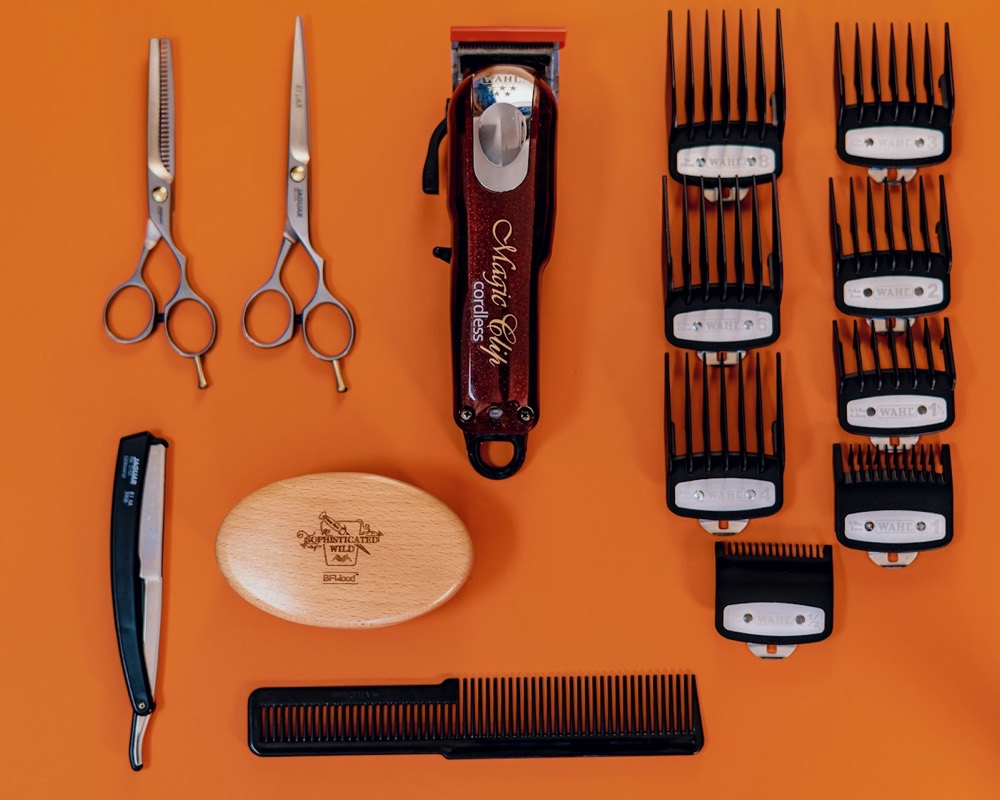 Clippers, scissors, combs and a straight razor laid out on an orange table